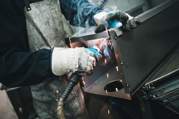 Metallurgy industry. Factory for production of heavy pellet stoves and boilers. Manual worker welder on his job. Extremely dark conditions and visible noise. Focus on foreground.