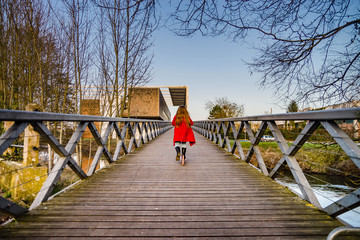 Little girl skating on the long wooden bridge over the river