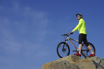 Fototapeta na wymiar Smile man, in light-green jacket and red sneakers, near mountain bike with sky background