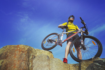 Fototapeta na wymiar Man, in yellow t-shirt and red sneakers, near mountain bike with sky background.