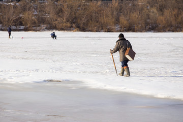 A fisherman on the river walks through dangerous thin ice. The danger of falling under the ice. Near the water from melted ice