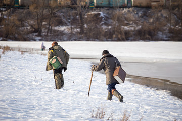 Two fishermen walk through the snow for winter fishing along the river bank