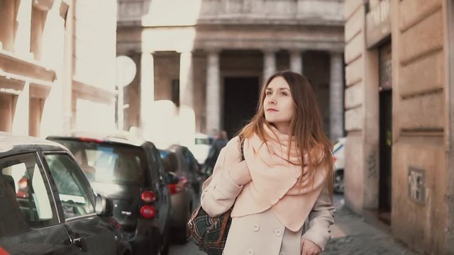 Portrait of young stylish woman walking in the city centre. Inspired and happy girl explores the old streets of the city