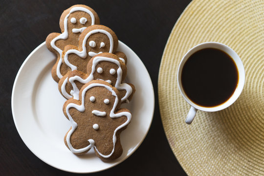gingerbread men on a white plate on black background with a cup coffee