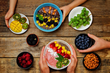 Men's and kid's hands with healthy breakfast smoothie bowls with fruits and berries