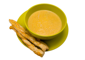 Yellow pumpkin soup in a green plate and crispy italian breadsticks isolated on white