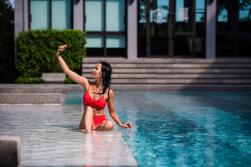 Beautiful woman in bikini taking a selfie by pool side on a sunny day at luxury hotel