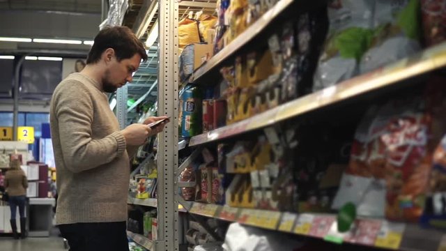 The dark-haired man chooses food for his dog or cat in the mall.