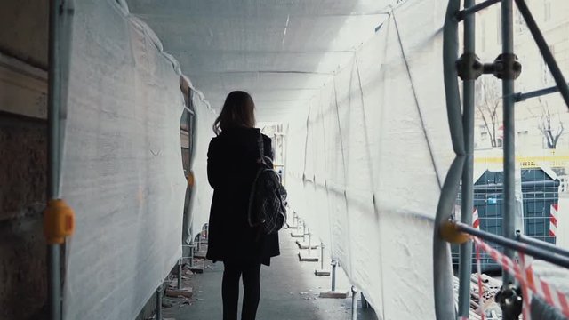 Student girl walking through the white construction corridor. Back view of young woman goes to work across the building.