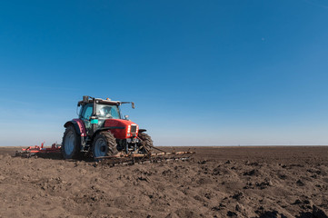 Fototapeta premium Farmer in tractor preparing land with seedbed cultivator in spring