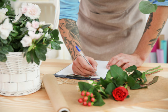 Tattooed florist writing down order on clipboard, closeup