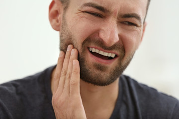 Handsome man suffering from toothache at home, closeup