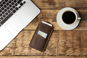 Leather case with mobile phone, laptop and cup of coffee on wooden table