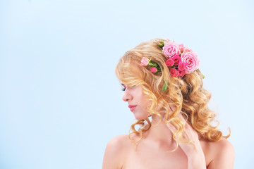 Beautiful young woman with flowers in hair on light background