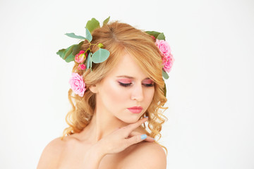 Beautiful young woman with flowers in hair on white background