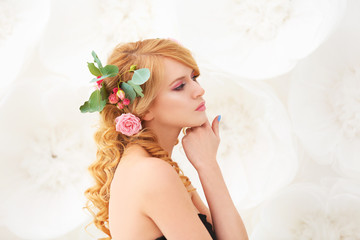 Beautiful young woman with flowers in hair on light background