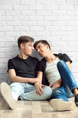 Fototapeta na wymiar Happy gay couple sitting on white brick wall background
