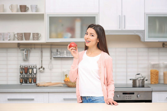 Beautiful young woman with apple in kitchen