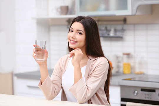 Beautiful young woman with glass of water in kitchen