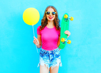 Fashion pretty woman and yellow air balloon with skateboard having fun over colorful blue background