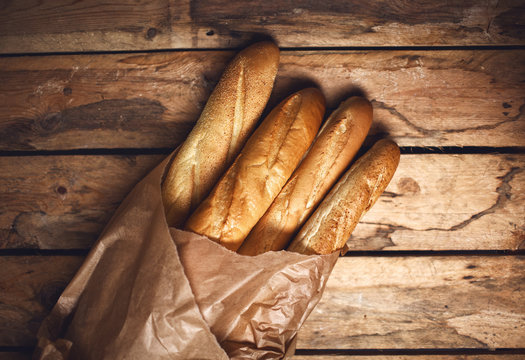 Four baguette bread loaves in paper bag on wooden background