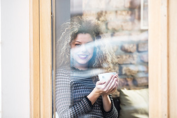 Portrait of a beautiful smiling young woman sitting indoors with a cup of warm drink