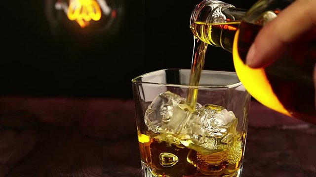 barman pouring whiskey with ice cubes on wood table, warm atmosphere, time of relax with whisky with some light warm vintage bulb on background