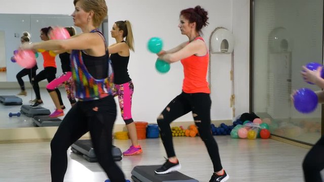 Women working out at the fitness club with stepper and balls in hands