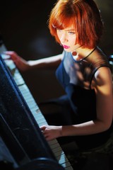 Portrait of a charming brown-haired girl with stylish hairstyle and perfect makeup in elegant black dress playing the piano in light, closeup.