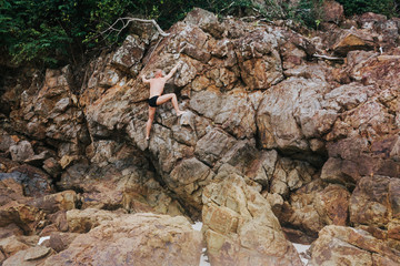 Man in beachwear climbing a rock. Back view of a man wearing swimwear Climbing on a rock. Horizontal outdoors shot.