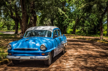 Obraz na płótnie Canvas HDR - Amerikanischer blauer Oldtimer parkt unter Bäumen in Santa Clara Kuba - Serie Kuba Reportage