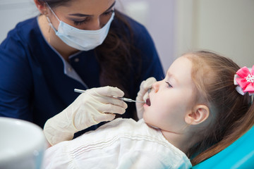 female dentist in mask treats teeth little girl
