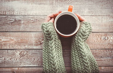Female hands holding cup of black tea on wooden background.  top view. Retro toning