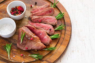 Roasted beef steak cut into slices with rosemary on wooden cutting board