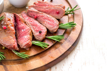 Roasted beef steak cut into slices with rosemary on wooden cutting board