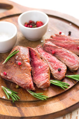 Roasted beef steak cut into slices with rosemary on wooden cutting board