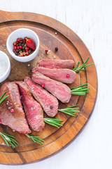 Roasted beef steak cut into slices with rosemary on wooden cutting board