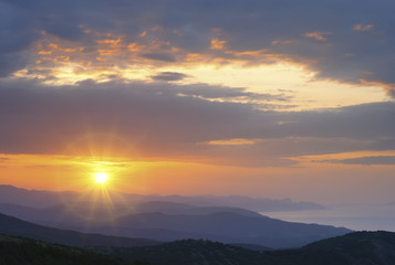 Mountain landscape at sunset. Amazing view from the mountain peak on rocks, low clouds, blue sky and sea in the evening. Colorful nature background.