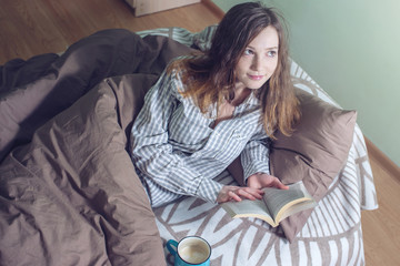Obraz premium Cute girl reading a book while lying in bed