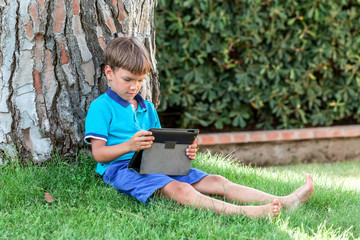 handsome happy boy sitting with tablet on green grass