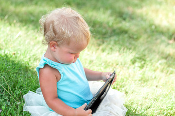 happy cute girl sittng with tablet on green grass