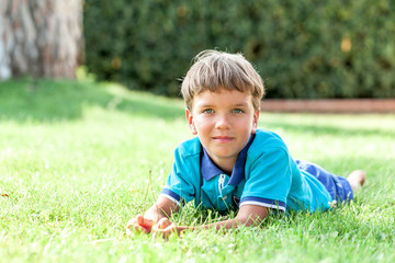 Happy boy lying on green grass in blue shirt in summer park