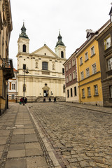 The area of the Old Town in Warsaw, Poland . An old street with nineteenth-century houses, a street lamp and a baroque church.
