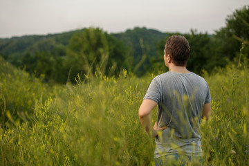 Naklejka na ściany i meble Man standing in the field looks at the beautiful landscape on nature. Copy space for your design