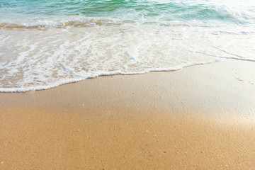 Fototapeta na wymiar Soft wave of blue ocean on sandy beach at sunny day. Background subject is soft focus