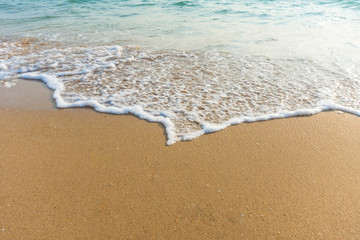 Fototapeta na wymiar Soft wave of blue ocean on sandy beach at sunny day. Background subject is soft focus