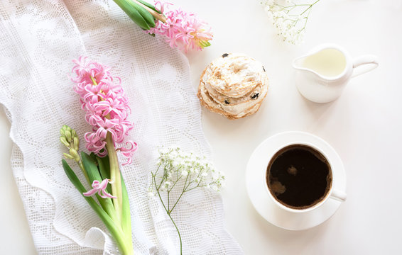 Morning romance breakfast, cup of coffee, milk jug and cake with decor of pink hyacinth. Spring concept. Top view.