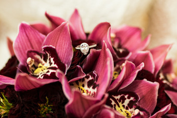 Ring with diamond lying on a wedding bouquets with red orchids. Wedding details