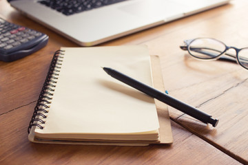 On wooden background notebook, pen and coffee.Workspace with laptop, working at home concept