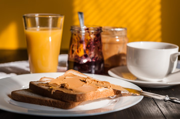 Breakfast with peanut butter and jam and a cup of coffee on a wooden table in the morning sun